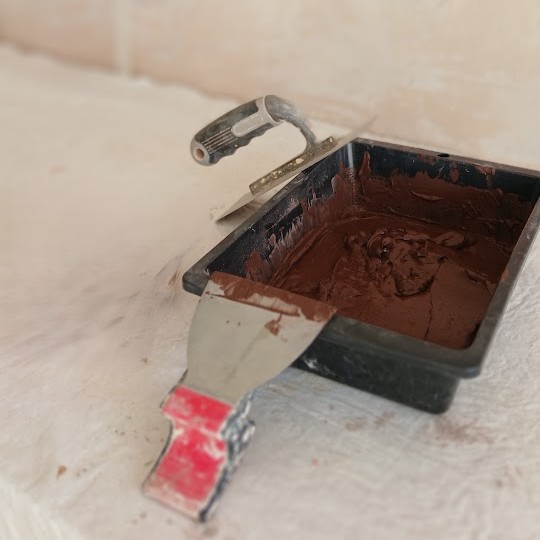 Bac contenant un enduit teinté brun et spatule pour la transformation d’un meuble.